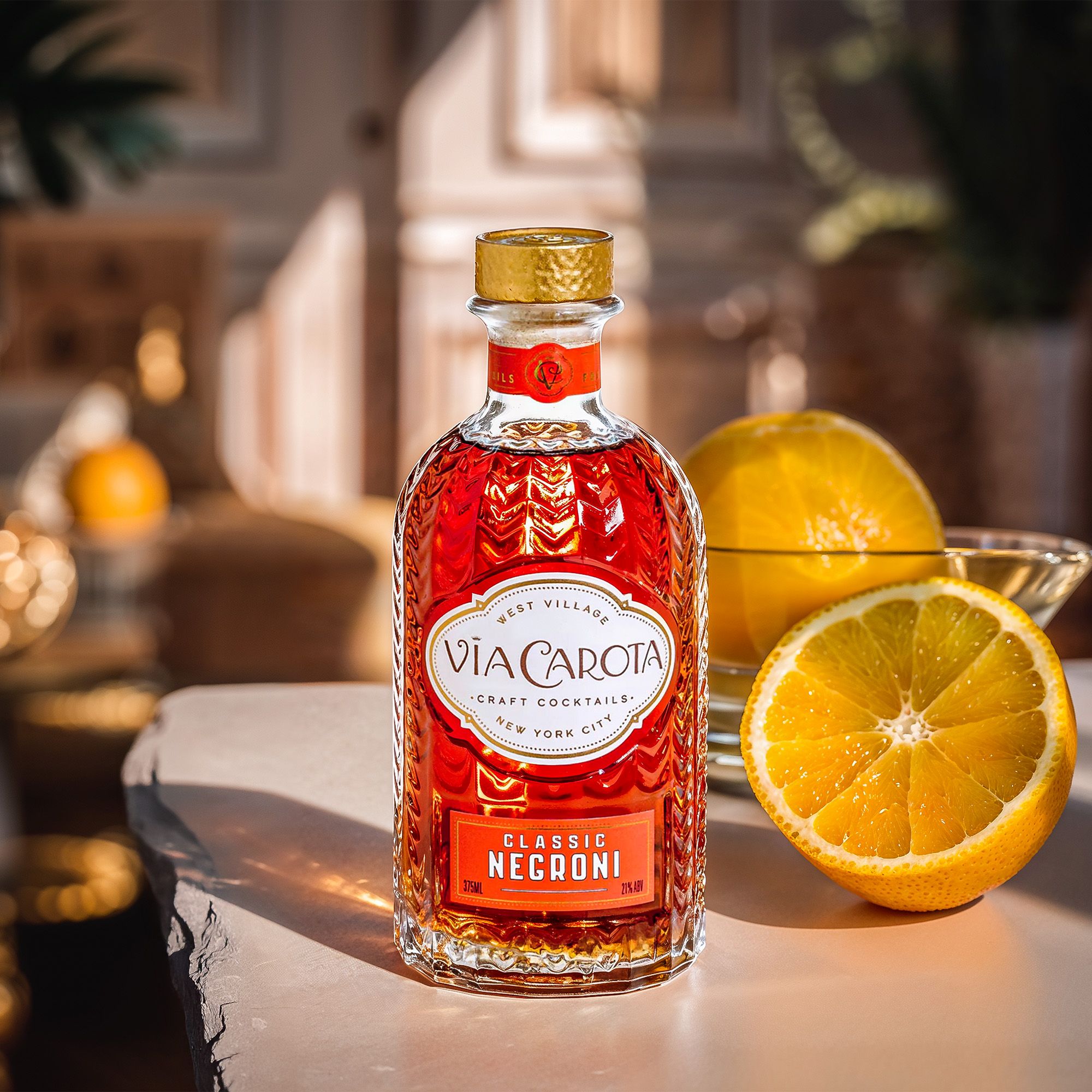Classic Negroni bottle in golden light with halved oranges and a coupe — Chronos Studio for Via Carota.