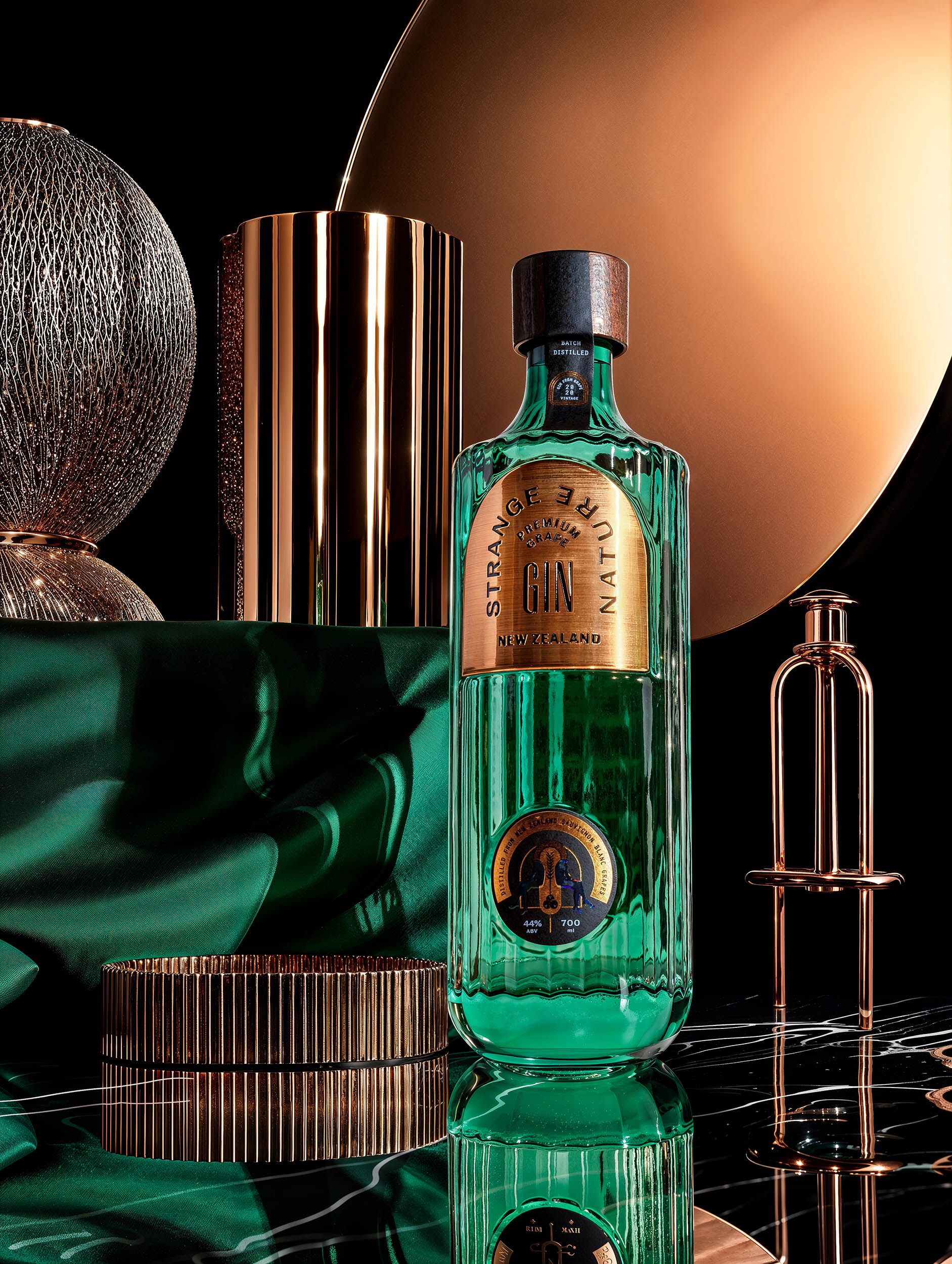 Portrait of the Strange Nature bottle against a copper disc, gold cylinder and emerald silk — Chronos Studio.