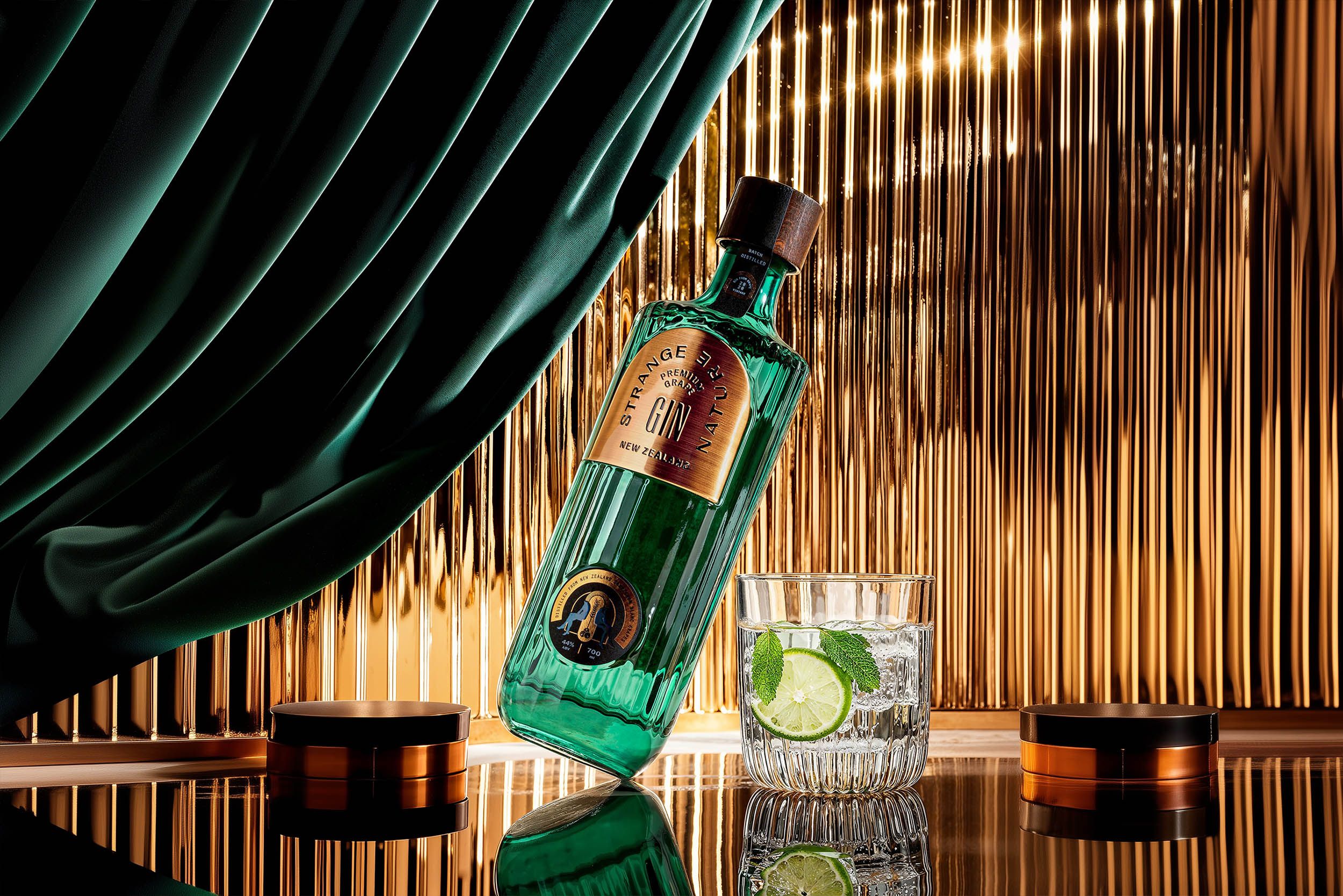 Strange Nature gin bottle leaning beside a gin and tonic against a gold ribbed backdrop with emerald drapery — Chronos Studio.