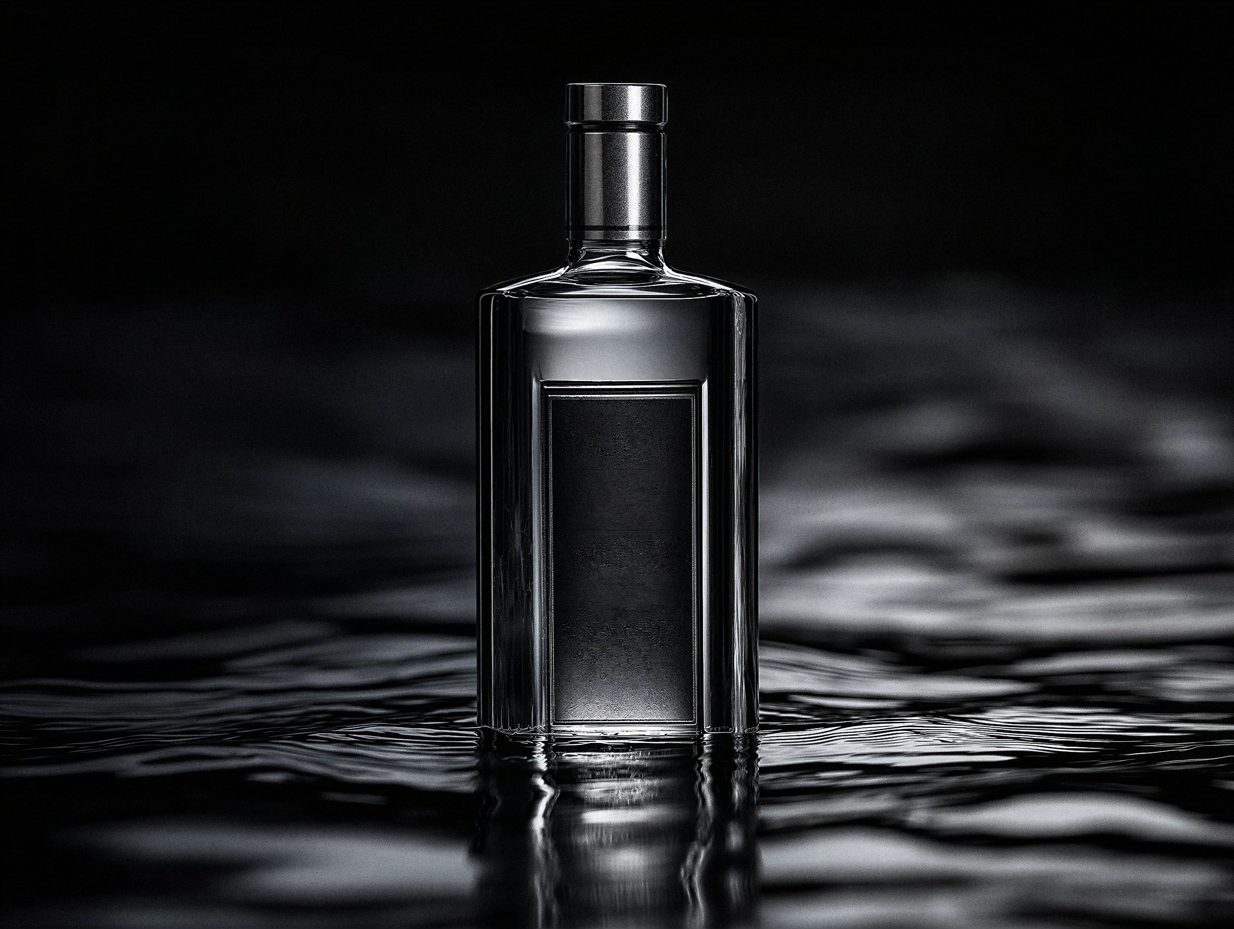 A clear minimalist spirits bottle standing in rippling water under dramatic dark lighting, reflected on the surface.