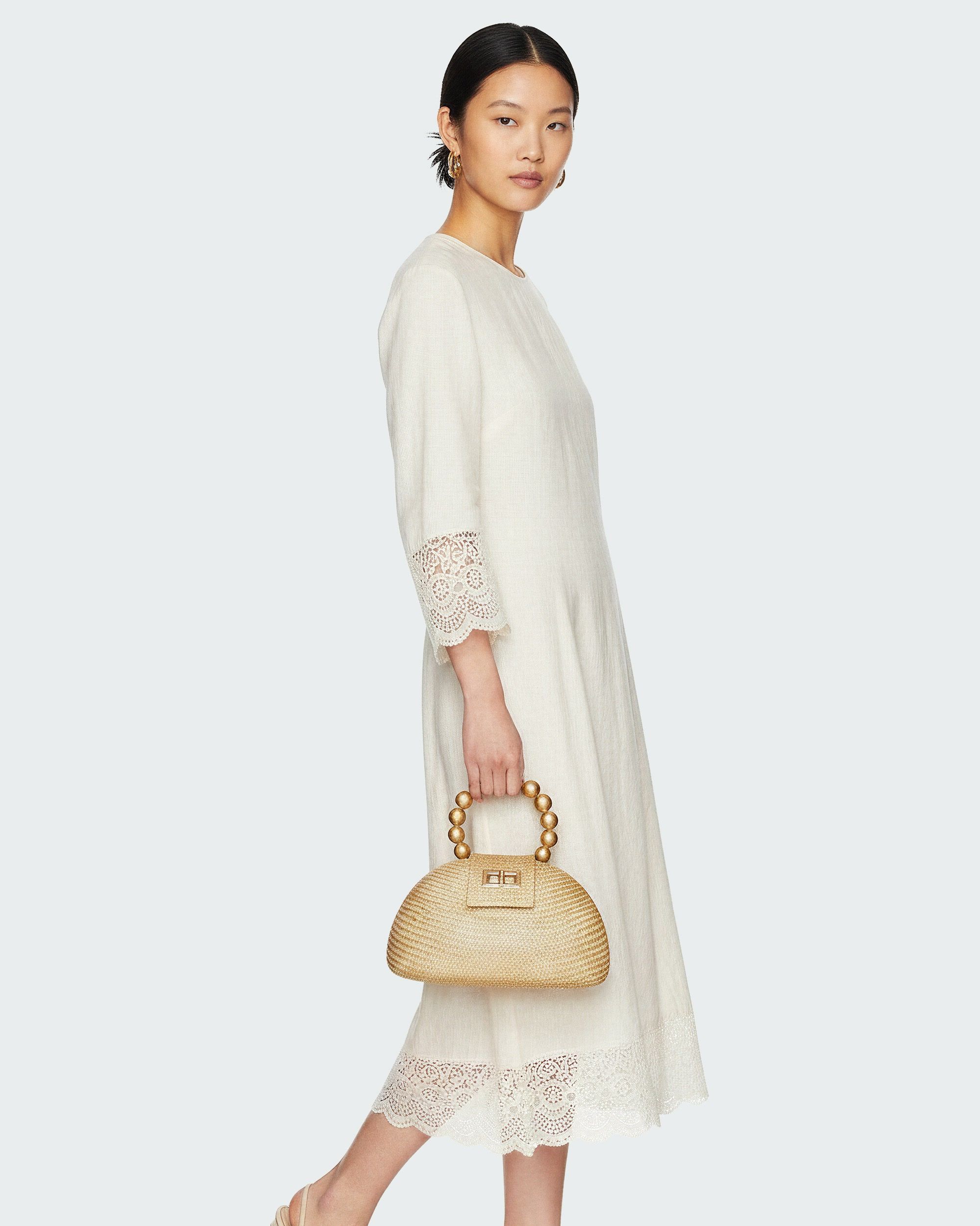 AI fashion photography of a model in a cream lace-trimmed dress holding a woven Soli & Sun handbag — Chronos Studio.