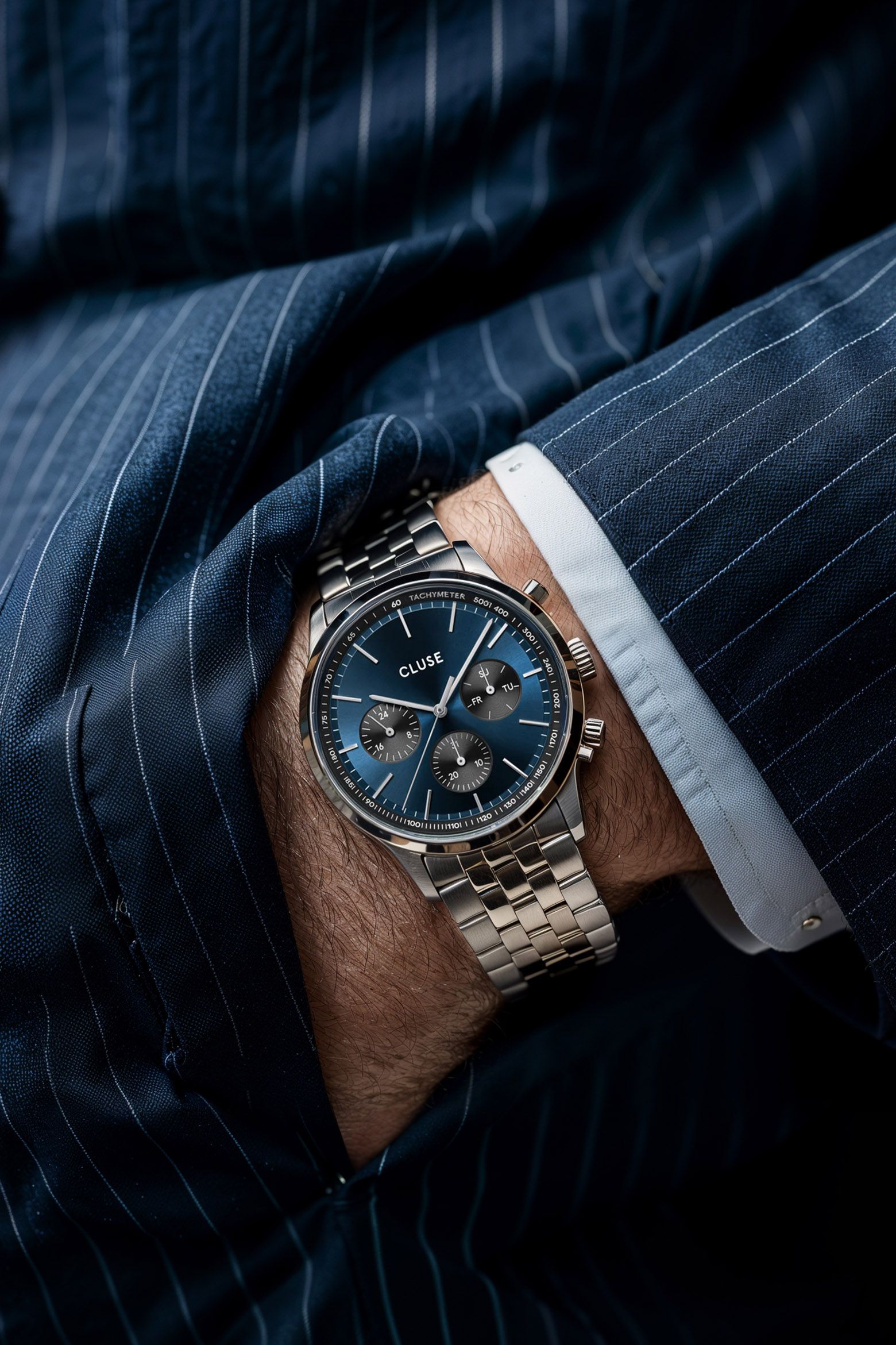 CLUSE navy chronograph worn at the cuff of a navy pinstripe suit — editorial wrist shot by Chronos Studio.