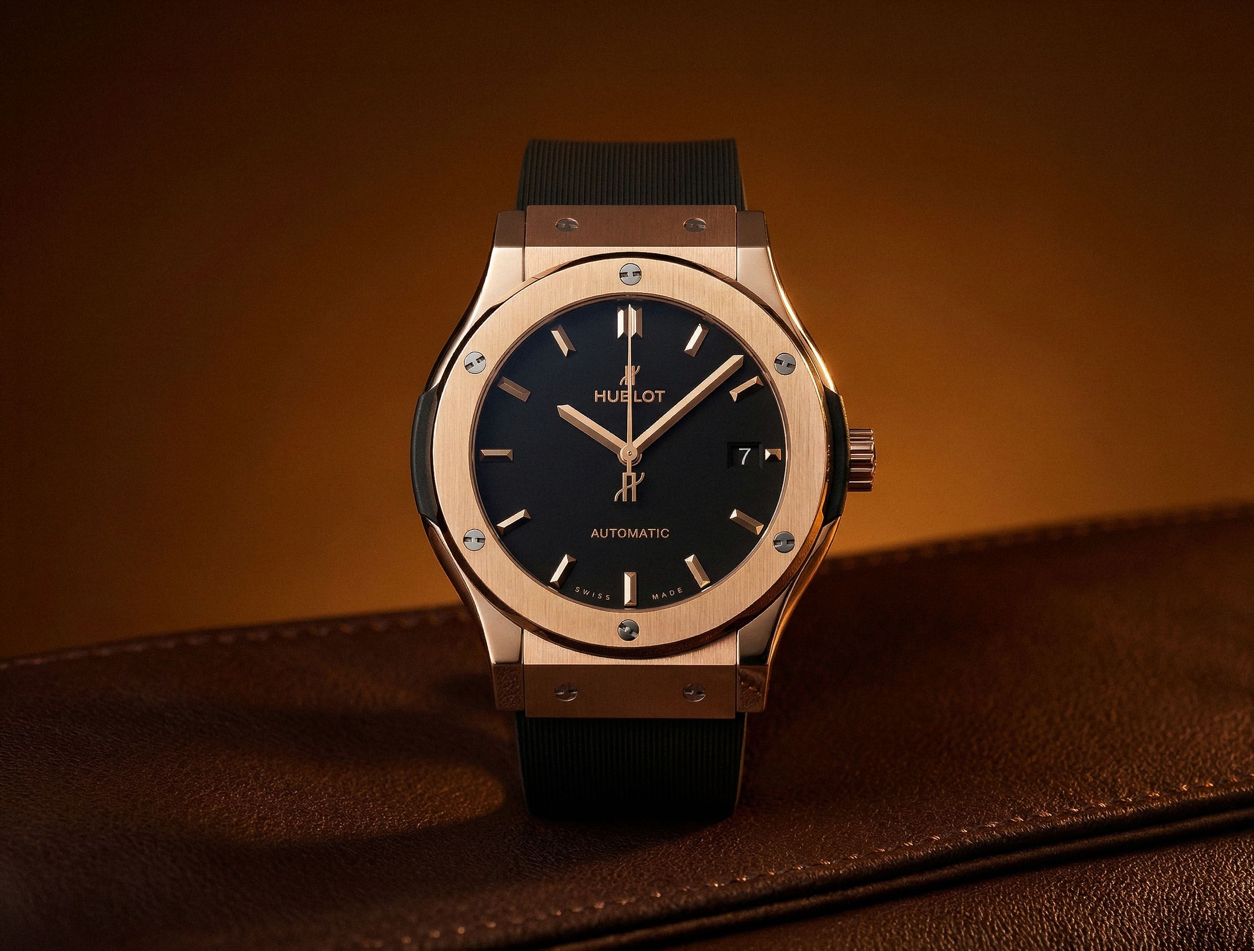 A rose-gold Hublot Classic Fusion automatic watch with a black dial on brown leather, lit with a warm amber glow.