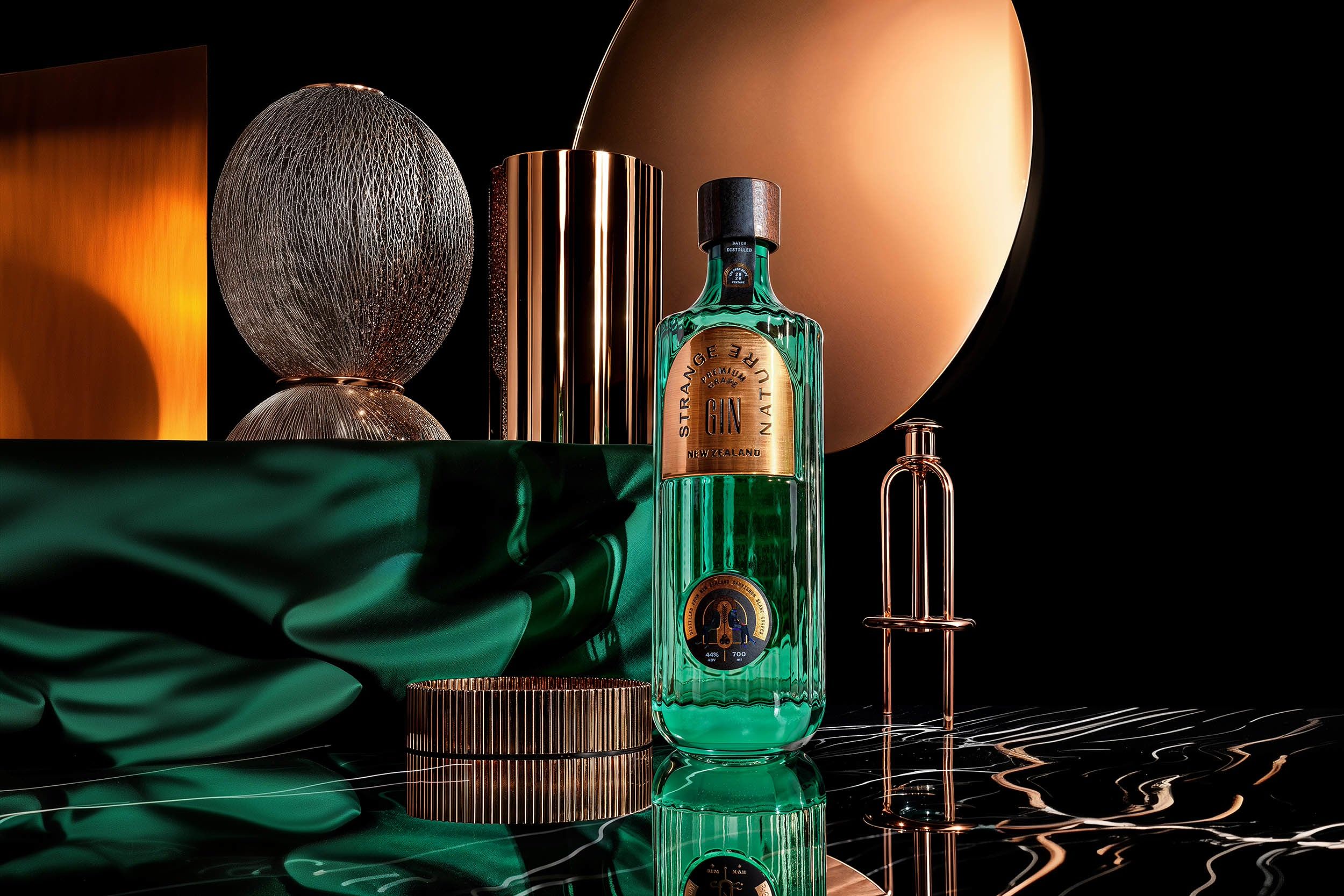 Strange Nature emerald gin bottle amid copper discs and green silk — case study by Chronos Studio.