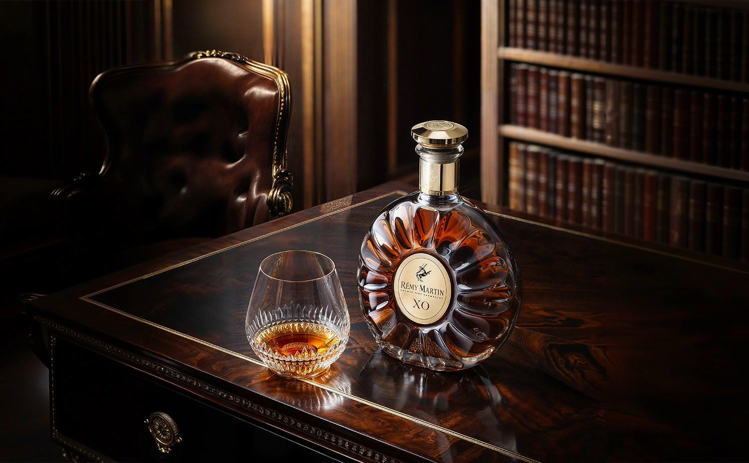 Rémy Martin XO decanter and crystal glass on a mahogany desk before a library — case study by Chronos Studio.