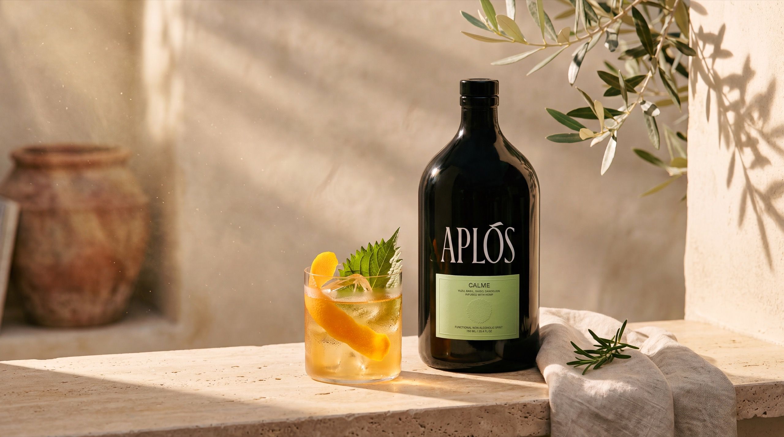 Aplós non-alcoholic spirit bottle and a mandarin-garnished serve on warm travertine, olive branch overhead in golden light — Style Study by Chronos Studio.