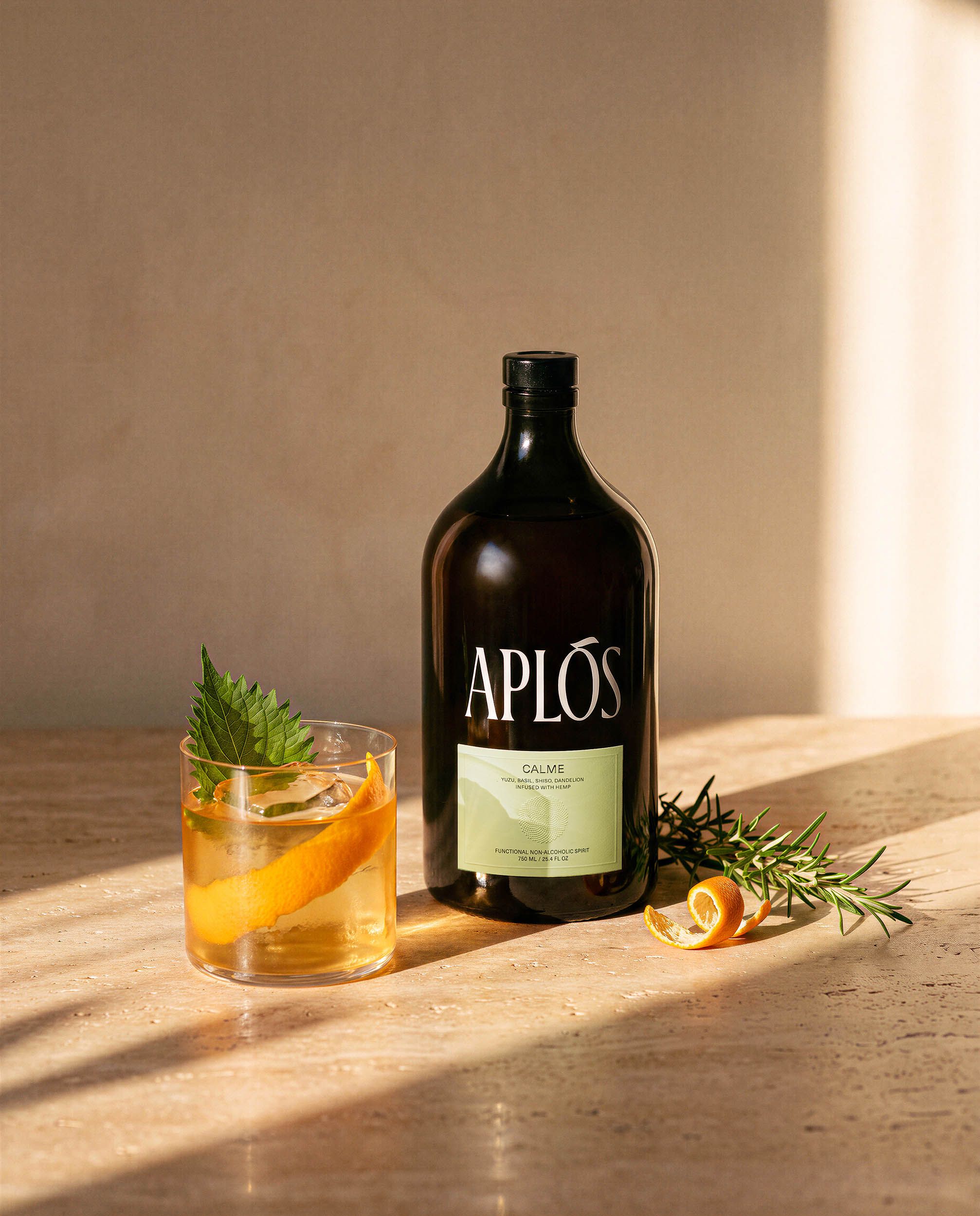 The Ritual — the Aplós bottle and a chilled lowball serve on honed travertine, long golden light bars and soft shadows falling across the stone.
