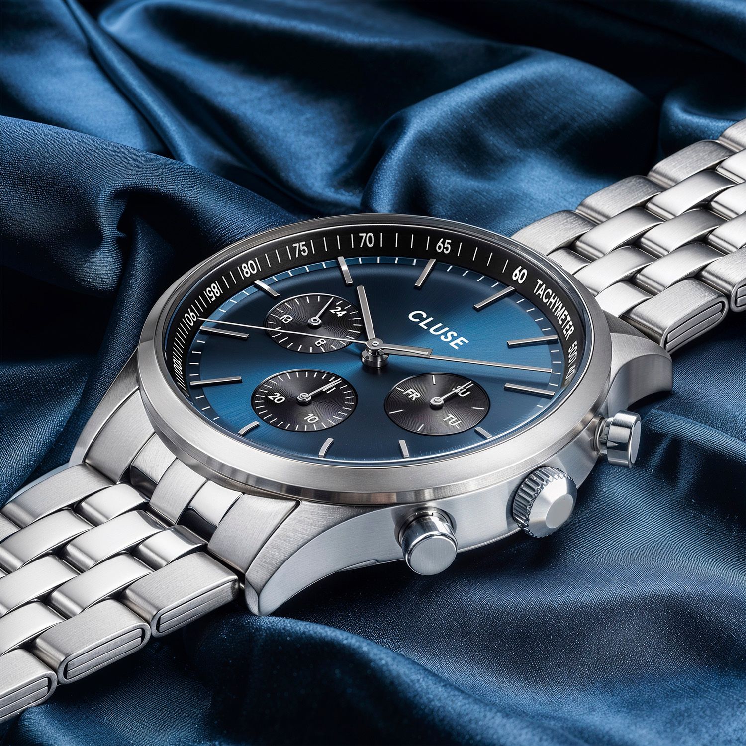 CLUSE navy chronograph on deep blue satin, square social post — Chronos Studio.