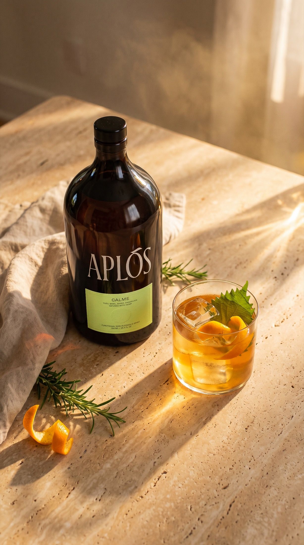 Vertical tablescape from above — the Aplós bottle, chilled serve, rosemary and mandarin peel on warm travertine in raking golden light.